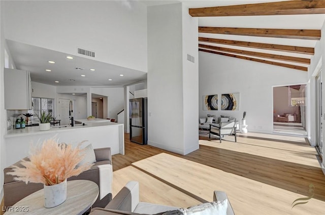 living room with beam ceiling, high vaulted ceiling, and light hardwood / wood-style flooring