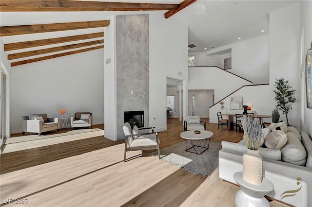 living room featuring beamed ceiling, high vaulted ceiling, a tiled fireplace, and hardwood / wood-style floors