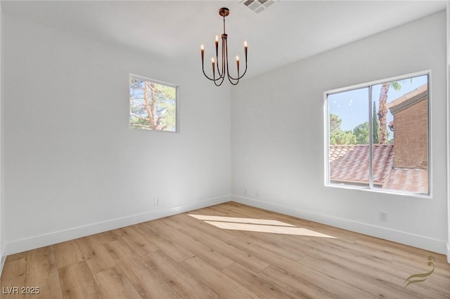 spare room featuring a notable chandelier and light wood-type flooring