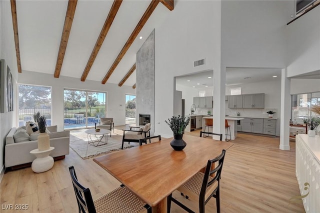 dining room with beamed ceiling, high vaulted ceiling, a large fireplace, and light wood-type flooring