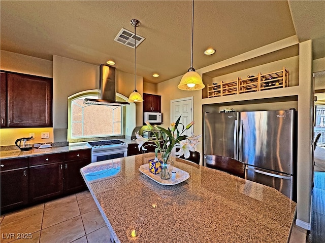 kitchen with a center island, hanging light fixtures, white appliances, light stone countertops, and wall chimney range hood