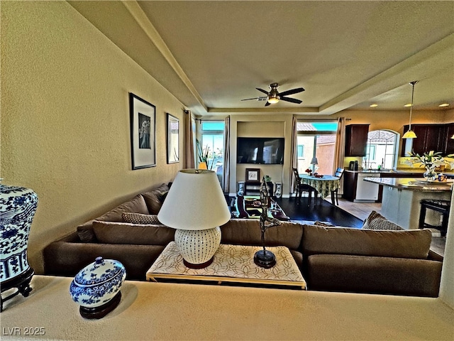 living room featuring ceiling fan and a raised ceiling