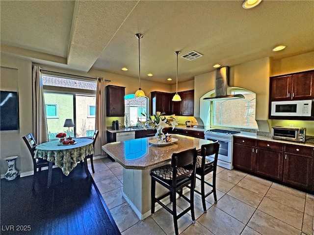 kitchen featuring decorative light fixtures, a center island, white appliances, light stone countertops, and wall chimney range hood