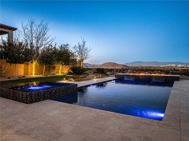 pool at dusk featuring a mountain view, a patio area, pool water feature, and an in ground hot tub