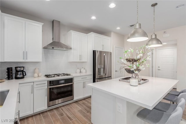 kitchen featuring pendant lighting, appliances with stainless steel finishes, wall chimney exhaust hood, and white cabinets