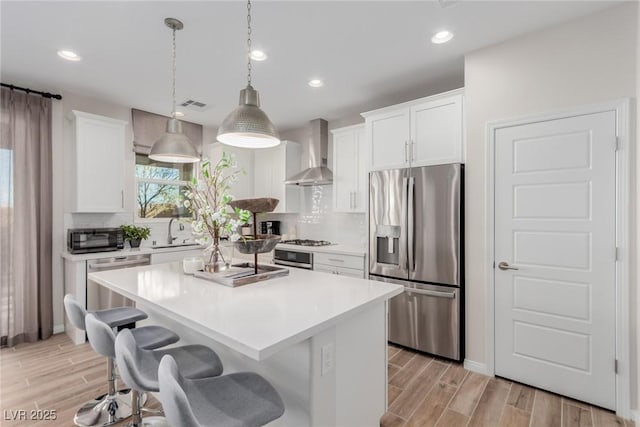 kitchen with wall chimney exhaust hood, appliances with stainless steel finishes, a center island, and white cabinets