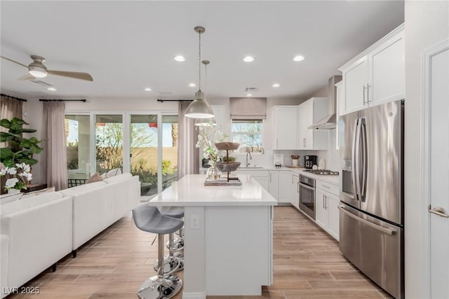 kitchen with white cabinetry, decorative light fixtures, a center island, ventilation hood, and stainless steel appliances