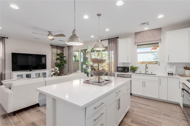 kitchen with sink, white cabinets, backsplash, hanging light fixtures, and a center island