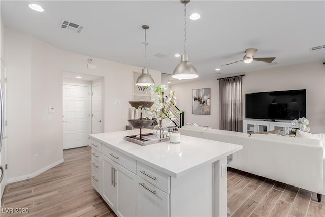 kitchen with a kitchen island, pendant lighting, white cabinetry, ceiling fan, and light hardwood / wood-style floors