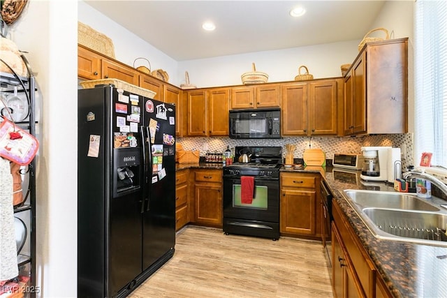 kitchen with sink, black appliances, dark stone countertops, light hardwood / wood-style floors, and backsplash