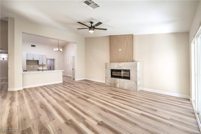 unfurnished living room with ceiling fan with notable chandelier, a fireplace, and light hardwood / wood-style floors