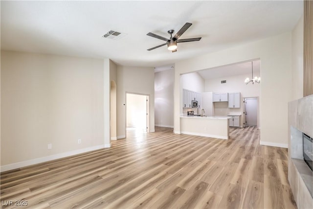 unfurnished living room with sink, vaulted ceiling, light wood-type flooring, a tile fireplace, and ceiling fan with notable chandelier