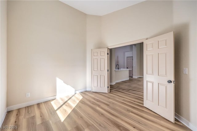 unfurnished room featuring a towering ceiling, sink, and light hardwood / wood-style flooring