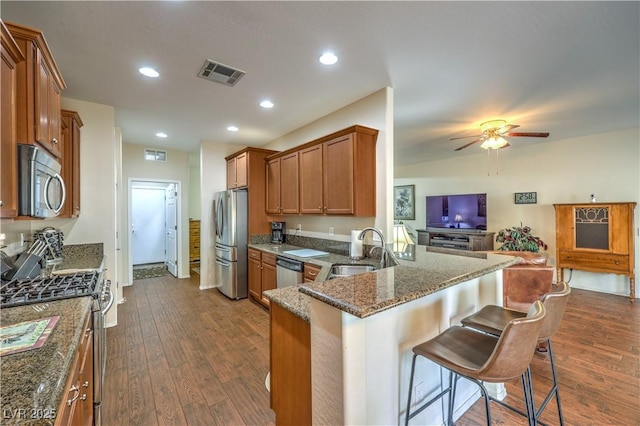 kitchen with sink, a breakfast bar, dark stone countertops, stainless steel appliances, and kitchen peninsula