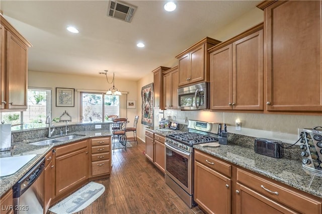 kitchen featuring appliances with stainless steel finishes, pendant lighting, sink, dark hardwood / wood-style flooring, and light stone countertops