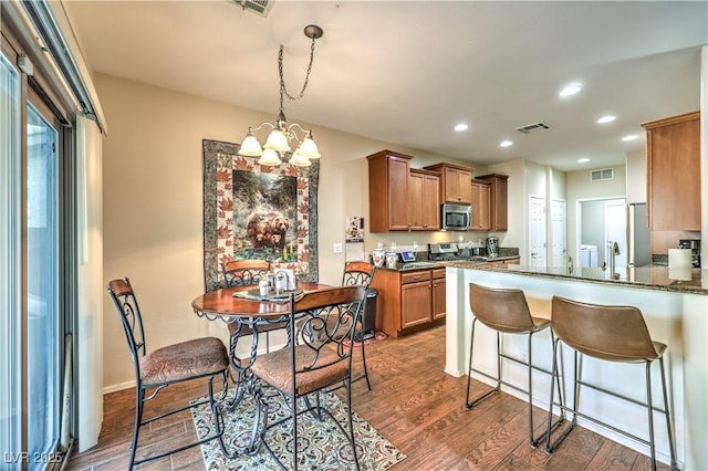 kitchen featuring dark wood-type flooring, dark stone countertops, appliances with stainless steel finishes, kitchen peninsula, and a notable chandelier