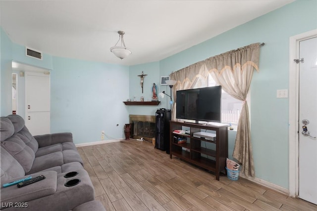 living room featuring a glass covered fireplace, wood finished floors, visible vents, and baseboards