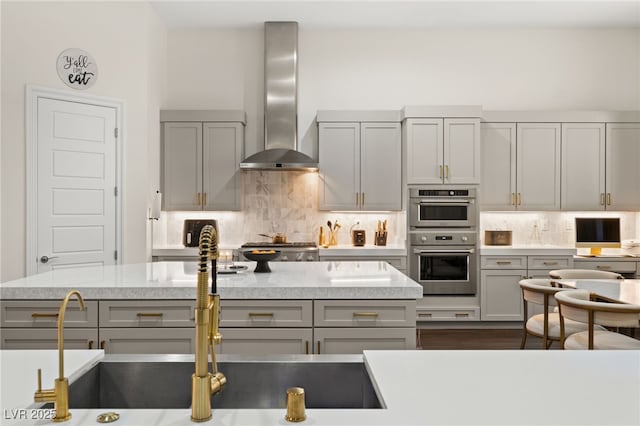 kitchen featuring tasteful backsplash, stainless steel double oven, wall chimney exhaust hood, and gray cabinets