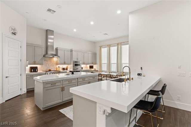 kitchen featuring wall chimney range hood, sink, tasteful backsplash, a kitchen bar, and kitchen peninsula