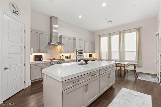 kitchen featuring a kitchen island, gray cabinetry, wall chimney range hood, and dark wood-type flooring