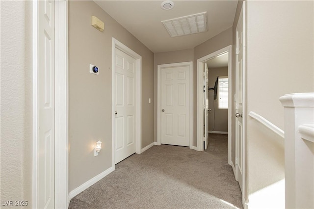 hall with baseboards, visible vents, and light colored carpet