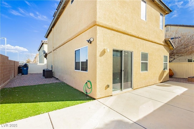 back of property with stucco siding, a lawn, central AC unit, a patio area, and a fenced backyard