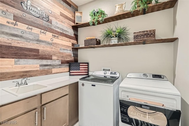 clothes washing area with cabinets, sink, washer and clothes dryer, and wood walls