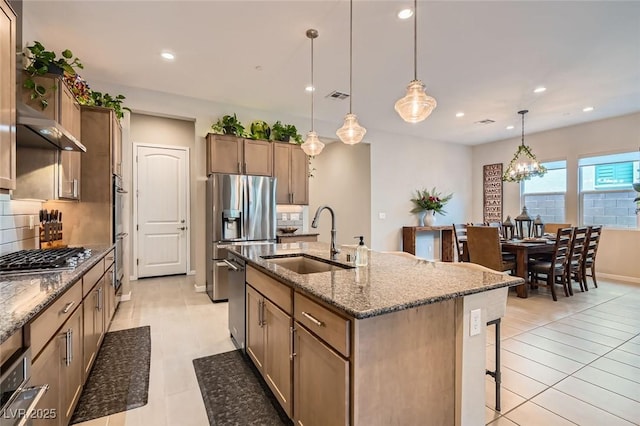 kitchen featuring appliances with stainless steel finishes, decorative light fixtures, sink, dark stone countertops, and a kitchen island with sink