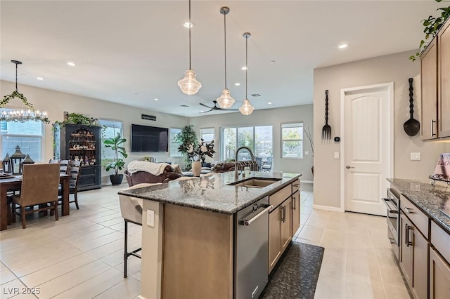 kitchen featuring sink, dark stone countertops, stainless steel dishwasher, an island with sink, and pendant lighting