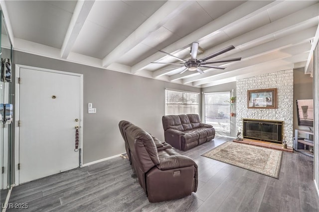 living room with dark wood-type flooring, ceiling fan, a fireplace, and beamed ceiling