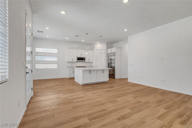 kitchen with white cabinetry, hanging light fixtures, a center island with sink, light hardwood / wood-style flooring, and appliances with stainless steel finishes