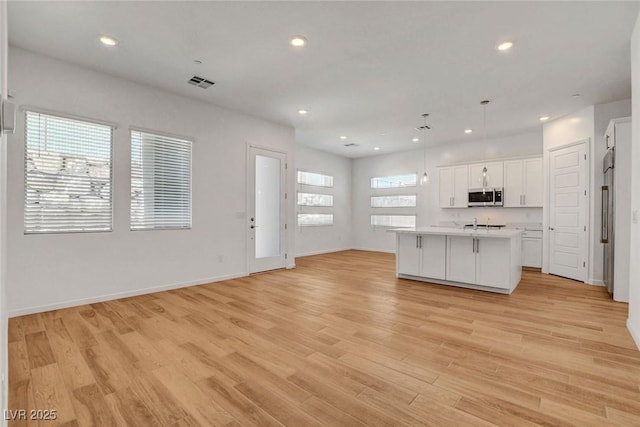 kitchen with an island with sink, light hardwood / wood-style flooring, white cabinets, and decorative light fixtures