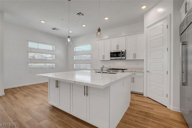 kitchen with sink, a kitchen island with sink, and white cabinets