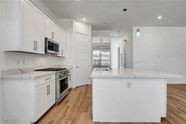 kitchen featuring sink, high end appliances, a center island with sink, pendant lighting, and white cabinets