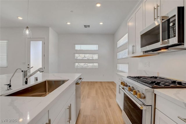 kitchen featuring pendant lighting, sink, appliances with stainless steel finishes, white cabinetry, and light stone counters