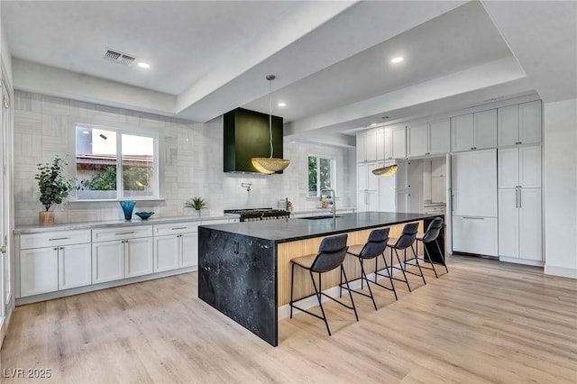 kitchen featuring sink, white cabinetry, a center island with sink, light hardwood / wood-style flooring, and paneled refrigerator