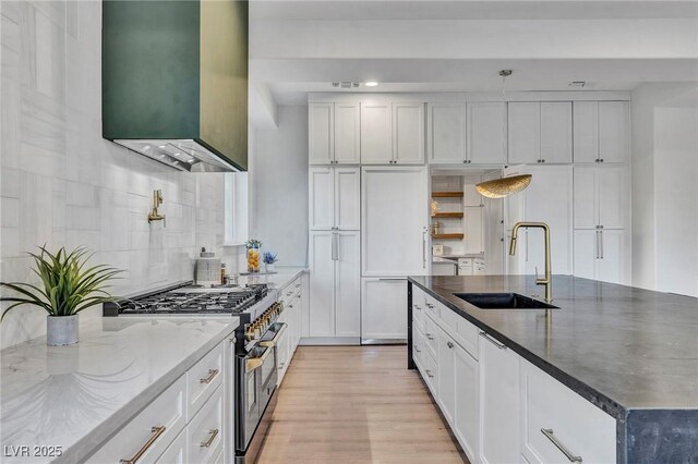 kitchen with white cabinetry, sink, high end range, dark stone counters, and a kitchen island with sink