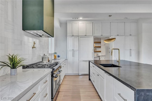 kitchen with a center island with sink, stainless steel range, white cabinets, dark stone counters, and a sink