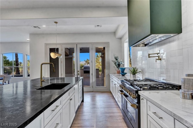 kitchen featuring range with two ovens, light stone counters, custom exhaust hood, white cabinetry, and a sink