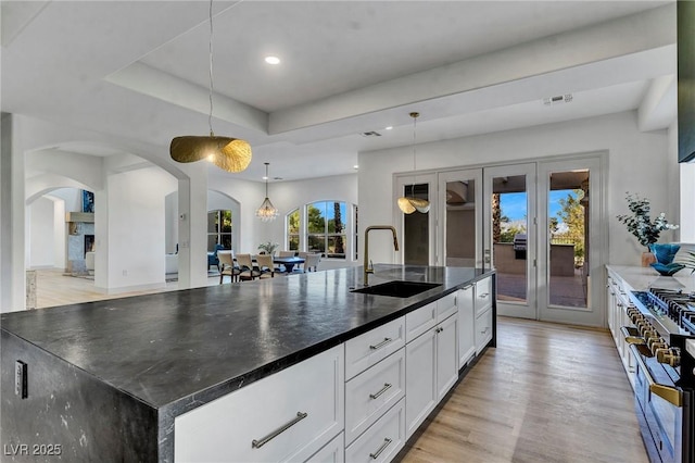 kitchen with sink, white cabinetry, decorative light fixtures, a center island with sink, and range with two ovens