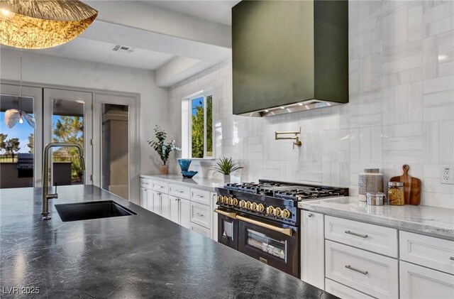 kitchen with sink, white cabinetry, double oven range, wall chimney range hood, and backsplash