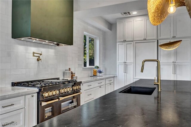 kitchen featuring tasteful backsplash, sink, white cabinets, and range with two ovens