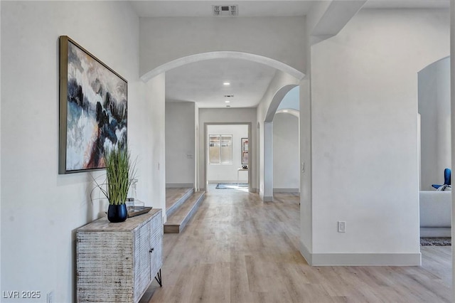 corridor with light wood finished floors, baseboards, visible vents, and arched walkways