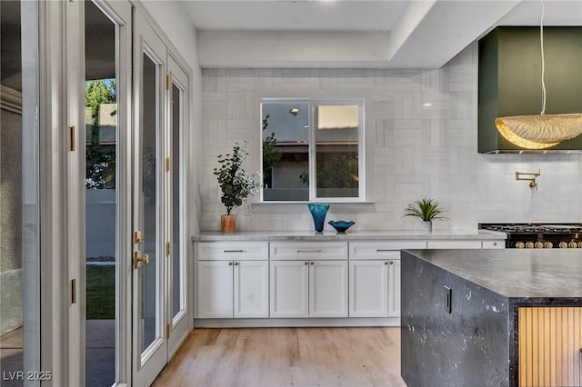 bar featuring light wood finished floors, decorative backsplash, wall chimney exhaust hood, stove, and pendant lighting