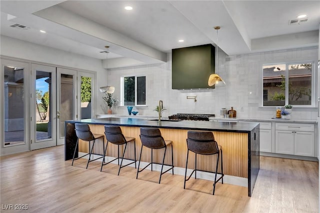 kitchen featuring backsplash, white cabinets, a kitchen bar, a kitchen island with sink, and light wood-type flooring