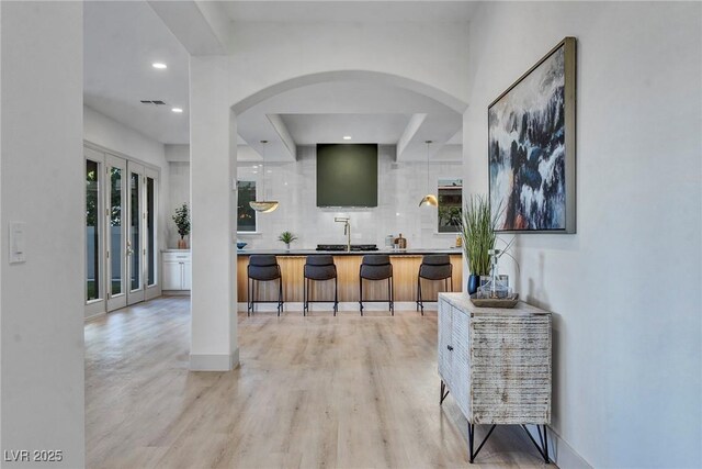 bar featuring tasteful backsplash, sink, light hardwood / wood-style floors, and decorative light fixtures