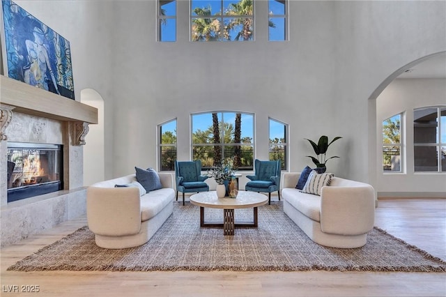 living room featuring a high end fireplace, arched walkways, a high ceiling, and wood finished floors