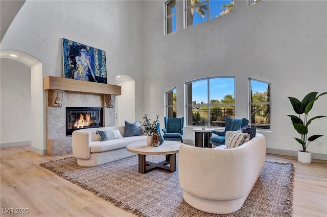 living area featuring baseboards, arched walkways, wood finished floors, and a glass covered fireplace