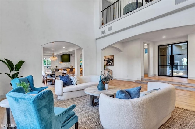 living area with arched walkways, a notable chandelier, wood finished floors, a towering ceiling, and baseboards