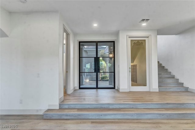 interior space with light wood-style flooring, visible vents, stairway, and baseboards